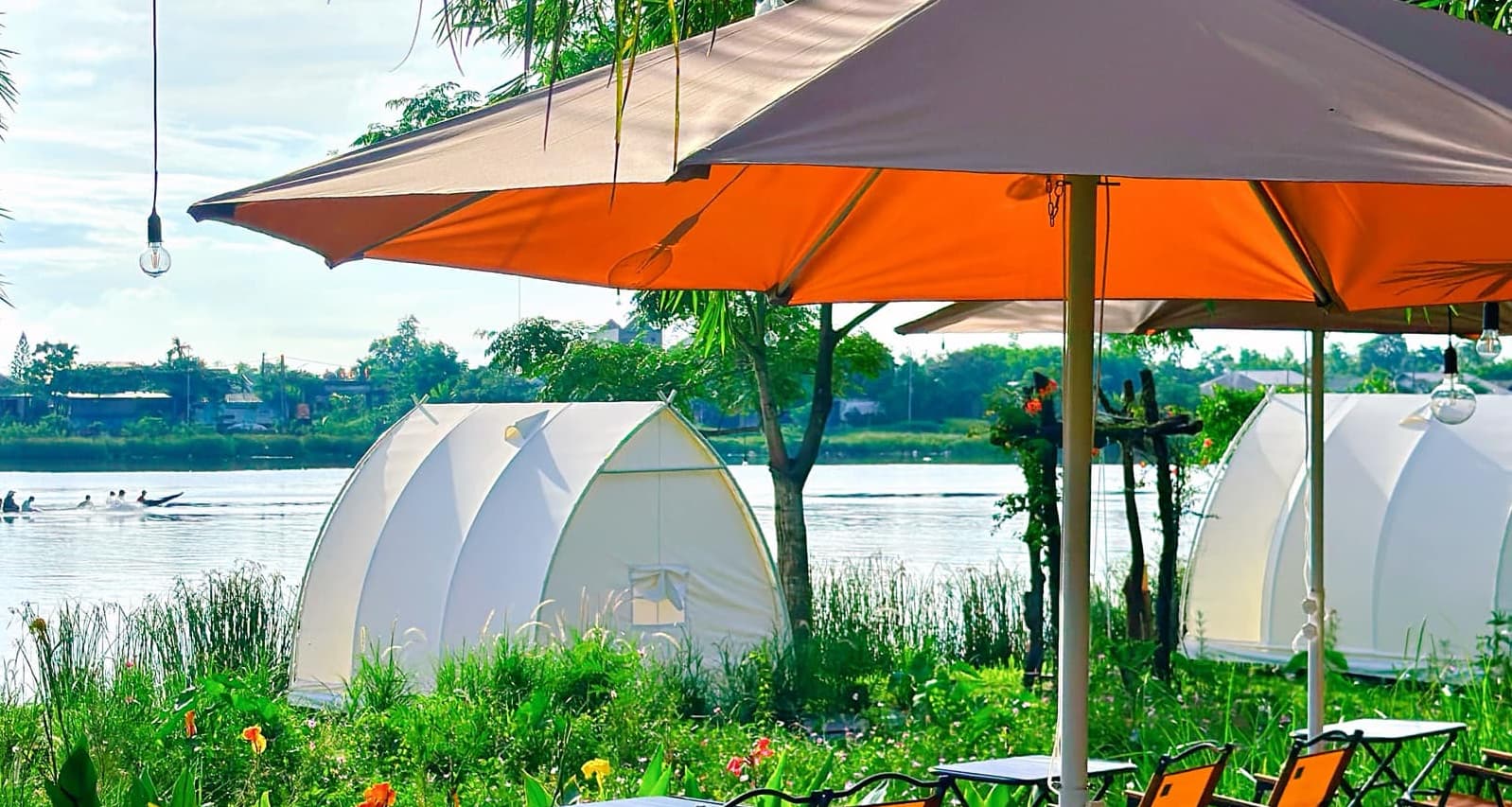 Góc ngồi dưới bóng dù bên bờ sông Hương — Dãy lều glamping và mặt nước